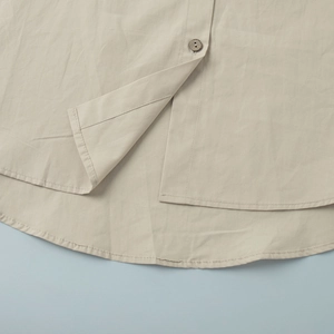 Detail of cotton shirt hem featuring a wooden button and clean curved stitching line