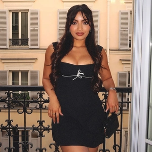 Detalle de un vestido corto negro ajustado con lazo blanco bordado en el escote cuadrado