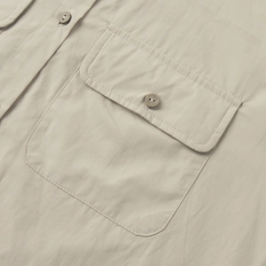 Detail of the cotton shirt's chest pocket with a wood-texture button and flap design