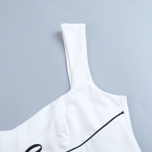 Detalle de vestido corto blanco con ribete negro, tirantes con lazo y diseño impreso