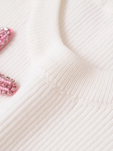Close-up of white ribbed knit fabric with delicate pink 3D beaded flower embroidery