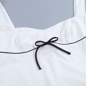 Detalle de un vestido blanco con escote cuadrado, ribete negro y un pequeño lazo frontal