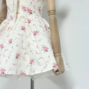 Detail eines cremefarbenen A-Linien-Kleids mit rosa Rosen und weißem Spitzenbesatz am Saum