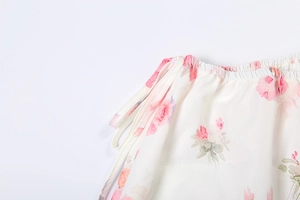 Detailed macro view of white floral dress featuring pink roses and adjustable waist ties