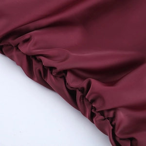 Detailed close-up of burgundy bow-tie dress fabric with shiny silk texture and ruching