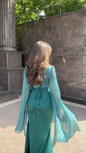 Detail of teal evening gown featuring a backless tie design and flowing fringe sleeves
