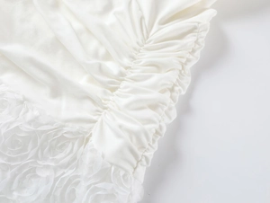 Detail of white dress featuring side ruching and delicate 3D floral lace trim
