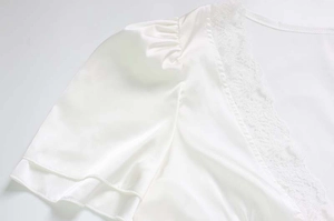 Dettaglio dell'abito in raso bianco con bordo in pizzo e maniche a sbuffo eleganti