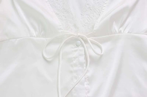 Dettaglio dell'abito in raso bianco con scollo a V in pizzo e bottoni decorativi