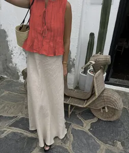 Outdoor shot of an elegant red sleeveless pleated top paired with a long beige linen skirt