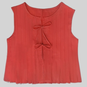 Detailed view of red sleeveless linen top featuring pleats and front bow tie closures