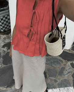 Detail of coral red pleated sleeveless linen top paired with beige linen skirt and straw bag