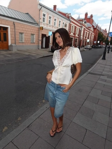 Elegante top in raso bianco con pizzo e gonna di jeans blu in un ambiente stradale esterno