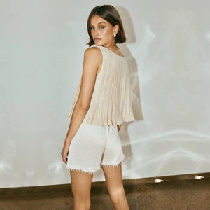 Detail showing elegant beige sleeveless pleated top with frayed edge white linen shorts
