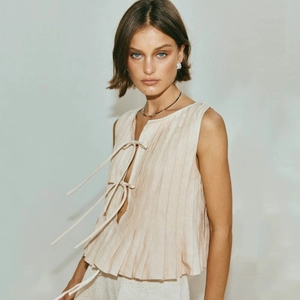Detail view of beige pleated sleeveless top featuring delicate front ribbon tie closures