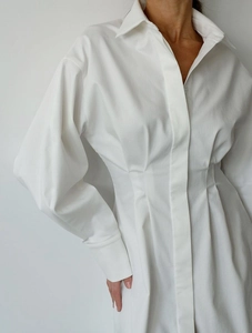 Gros plan d'une robe chemise évasée blanche avec des plis à la taille et poignets ajustés
