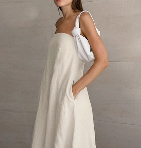 Detail of a minimalist ivory linen tube dress featuring side pockets and a knotted bag