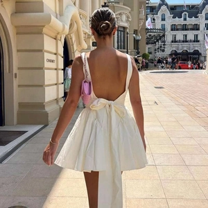 Robe blanche dos nu élégante avec grand nœud à la taille et jupe évasée dans une rue