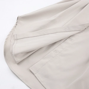 Détail de robe chemise beige avec boutons ronds, patte de boutonnage et ourlet arrondi