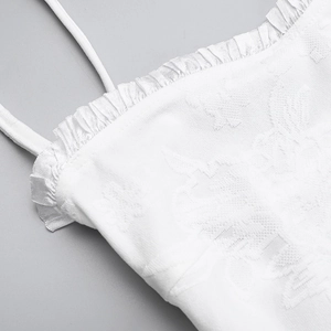 Macro shot of white jacquard fabric featuring delicate ruffles and thin shoulder straps