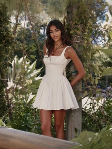 Mini robe blanche dos nu élégante avec nœud et jupe évasée dans un décor de jardin