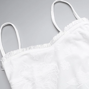 Detail of white spaghetti strap dress featuring delicate floral embroidery and ruffled trim