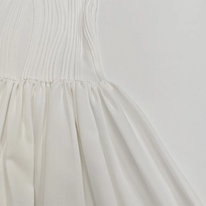 Détail d'une robe blanche présentant des plis verticaux et une texture de taille froncée