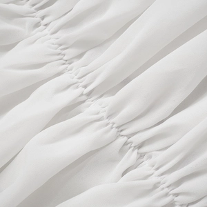 Primo piano del tessuto in chiffon bianco con texture pieghettata e dettagli semitrasparenti