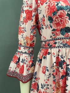 Détail d'une robe fleurie à manches évasées avec motif rose sur un tissu blanc cassé