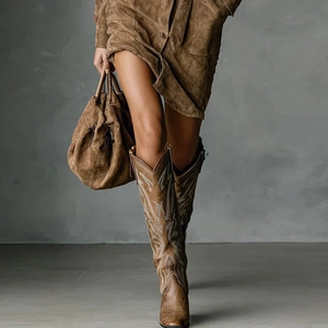 Close-up of brown suede cowboy boots with wave embroidery and autumn suede dress