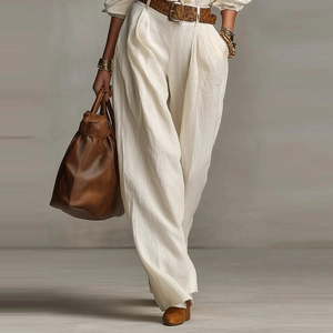 Detail of white wide-leg linen pants featuring high-waisted pleats and a brown leather belt