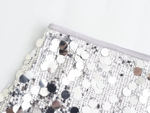 Détail de grandes paillettes argentées cousues sur le tissu d'une mini-jupe à taille haute