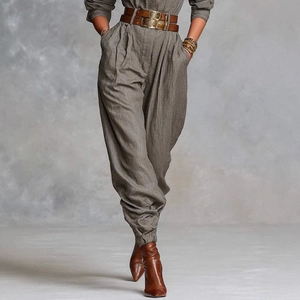 Detail view of high-waist pleated taupe trousers with a brown leather belt and gold buckle