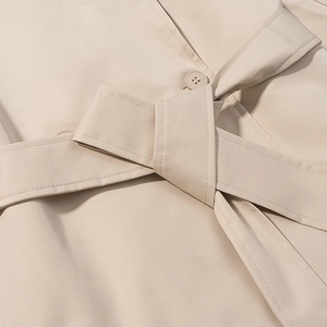 Dettaglio del nodo della cintura e trama del tessuto di un trench corto beige donna