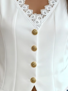 Détail d'un gilet blanc col en V avec dentelle délicate et boutons dorés texturés