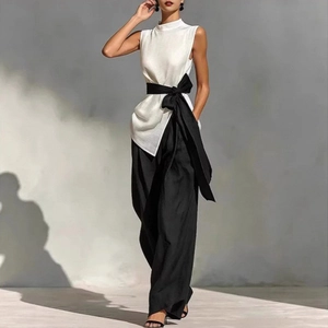 Detail of white sleeveless high neck top with a large black waist bow and wide leg trousers