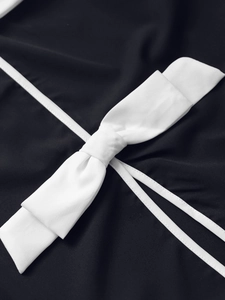 Detail of elegant white bow decoration and piping on a black polo style jacket