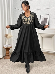 Close-up of golden floral embroidery and ruffled V-neck on a black long sleeve dress