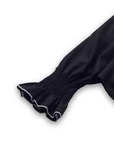 Detail of black sleeve with smocked cuffs and white contrast ruffle stitching