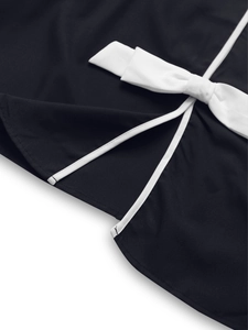 Close-up of black short jacket featuring a white bow detail and contrast piping on the hem