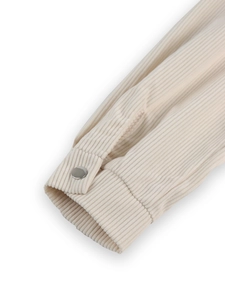 Detailed macro view of cream corduroy fabric texture and silver metal button on the cuff