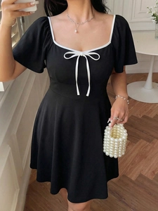Detailed view of the square neckline with white contrast trim and bow on a black dress