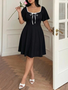 Detail of the square neckline with white contrast trim and a delicate bow tie on black dress