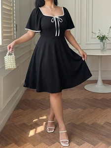 Detail of square neckline with white contrast trim and elegant bow on black A-line dress