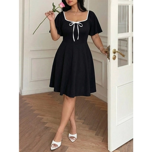 Elegant black A-line dress with white contrast square neck and bow detail in a home setting