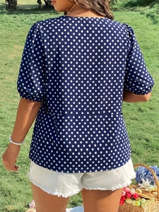 Back view of navy blue polka dot top with puff sleeves on model in outdoor setting