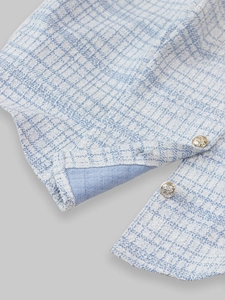 Close-up of light blue tweed jacket sleeve featuring ornate embossed gold metal buttons