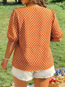 Outdoor back view of a burnt orange polka dot puff sleeve blouse in a garden setting
