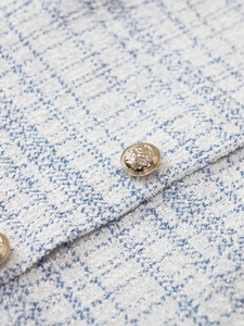 Macro shot of gold Medusa head embossed button on textured tweed fabric jacket