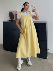 Detail of yellow striped overall dress featuring shoulder ties and functional side pockets